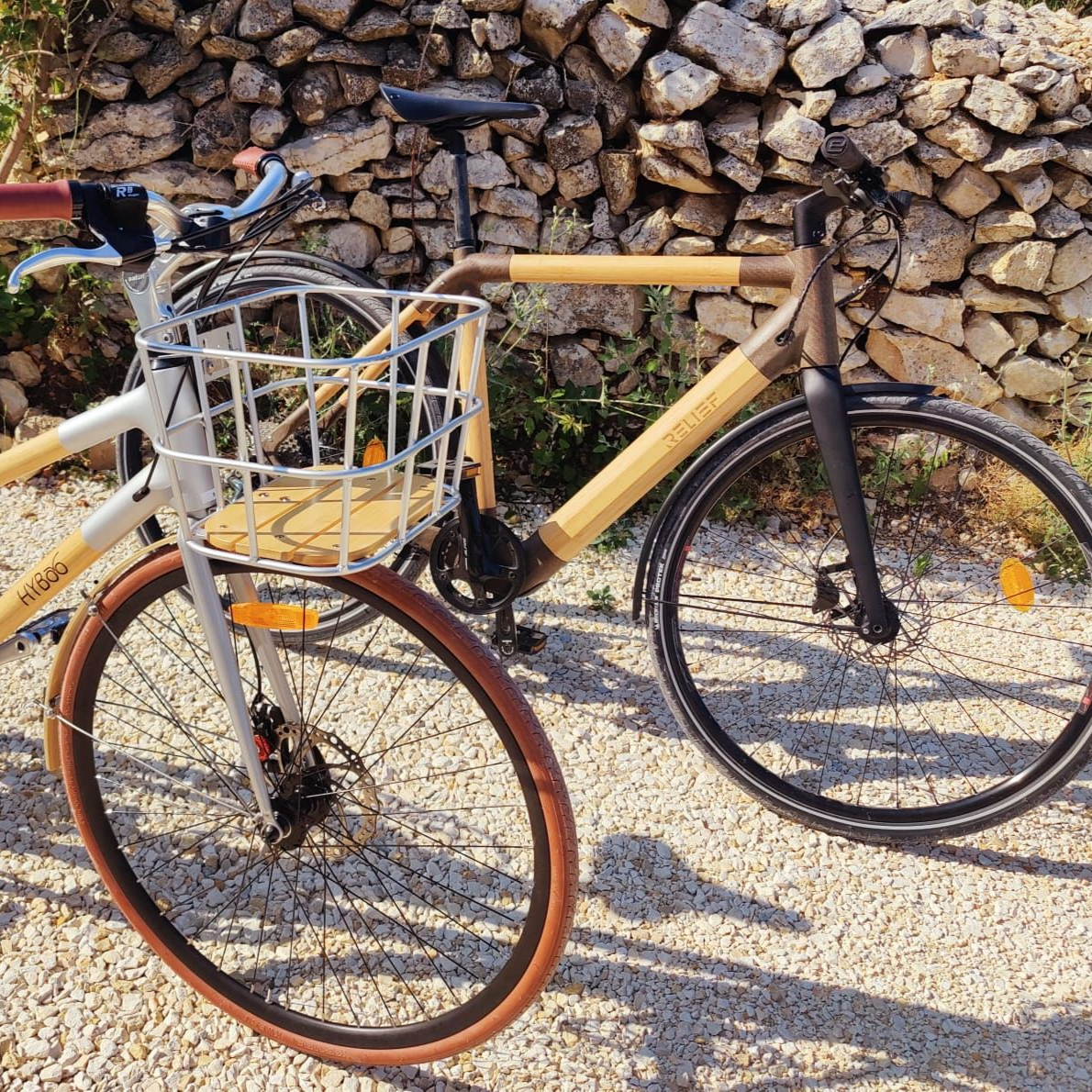 Deux vélos avec des cadres en bambou garés près d'un mur de pierre, l'un avec un panier avant et des pneus marron.