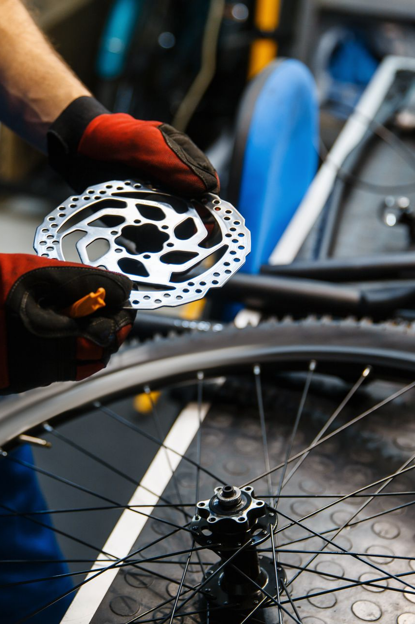 Une personne portant des gants rouges fixe un rotor de frein de vélo argenté à une roue.