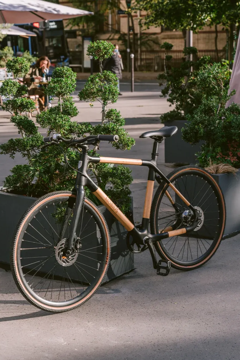 Vélo en bambou garé dans une rue de la ville, cadre noir et accents de bambou beige, près de la verdure.