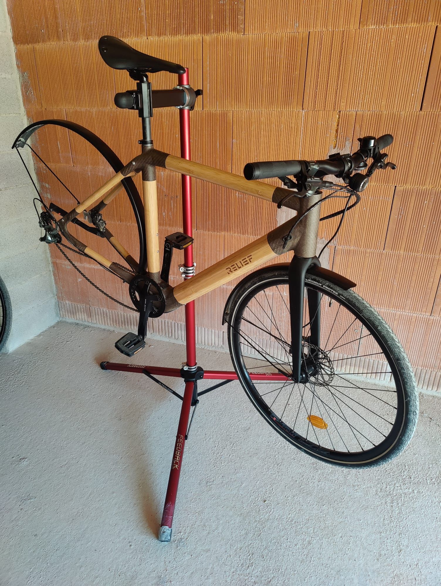 Vélo en bambou sur un support de réparation rouge contre un mur marron texturé.