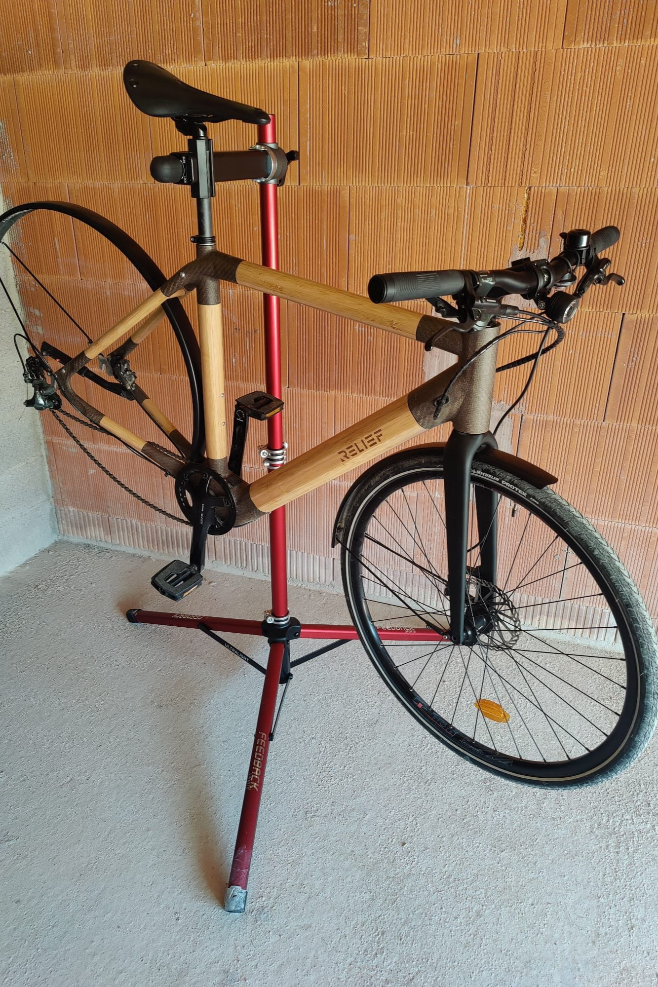 Vélo en bambou sur un support de réparation rouge contre un mur texturé.
