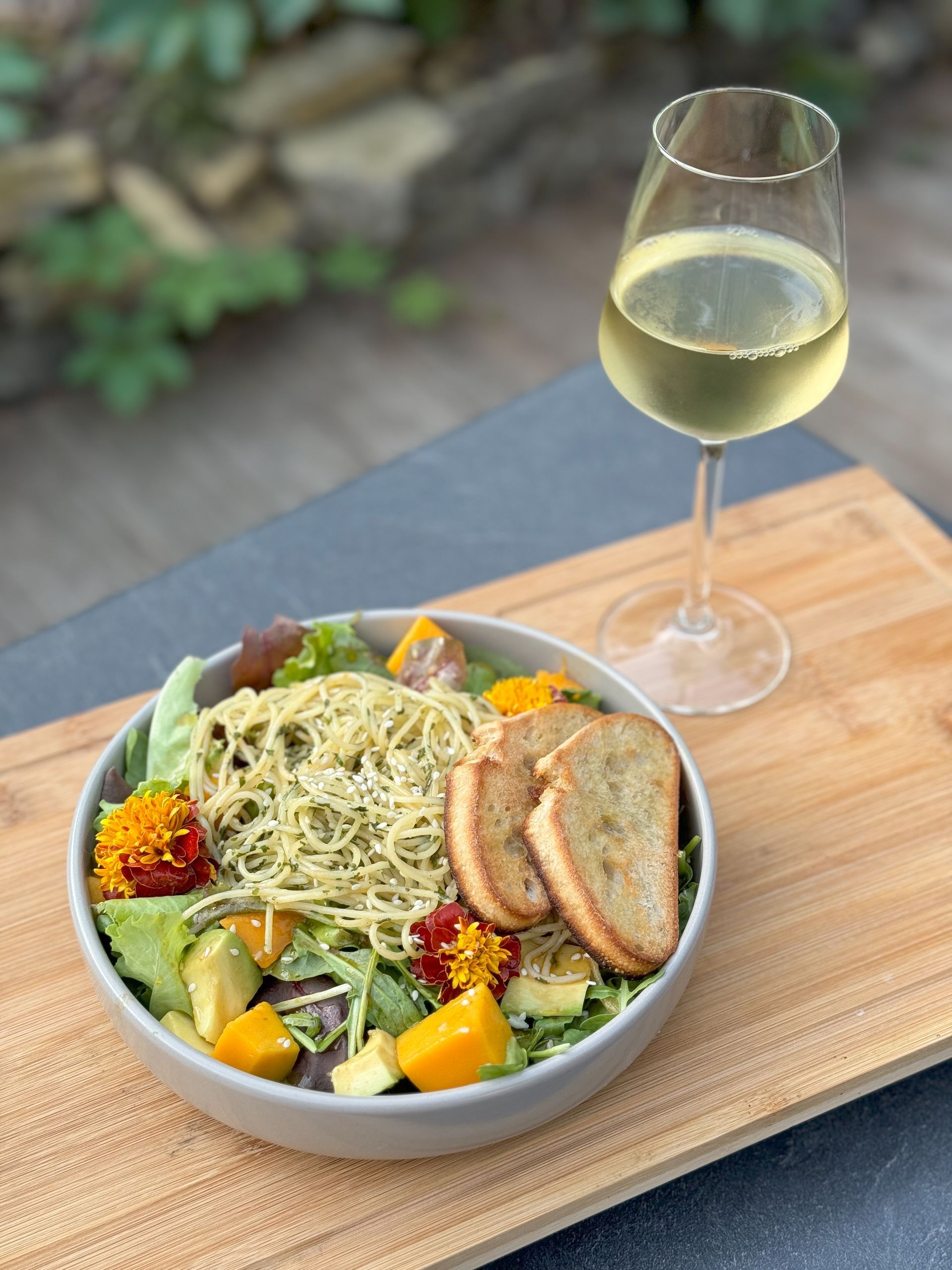 Eine Schüssel Salat und ein Glas Wein auf einem Holzschneidebrett.
