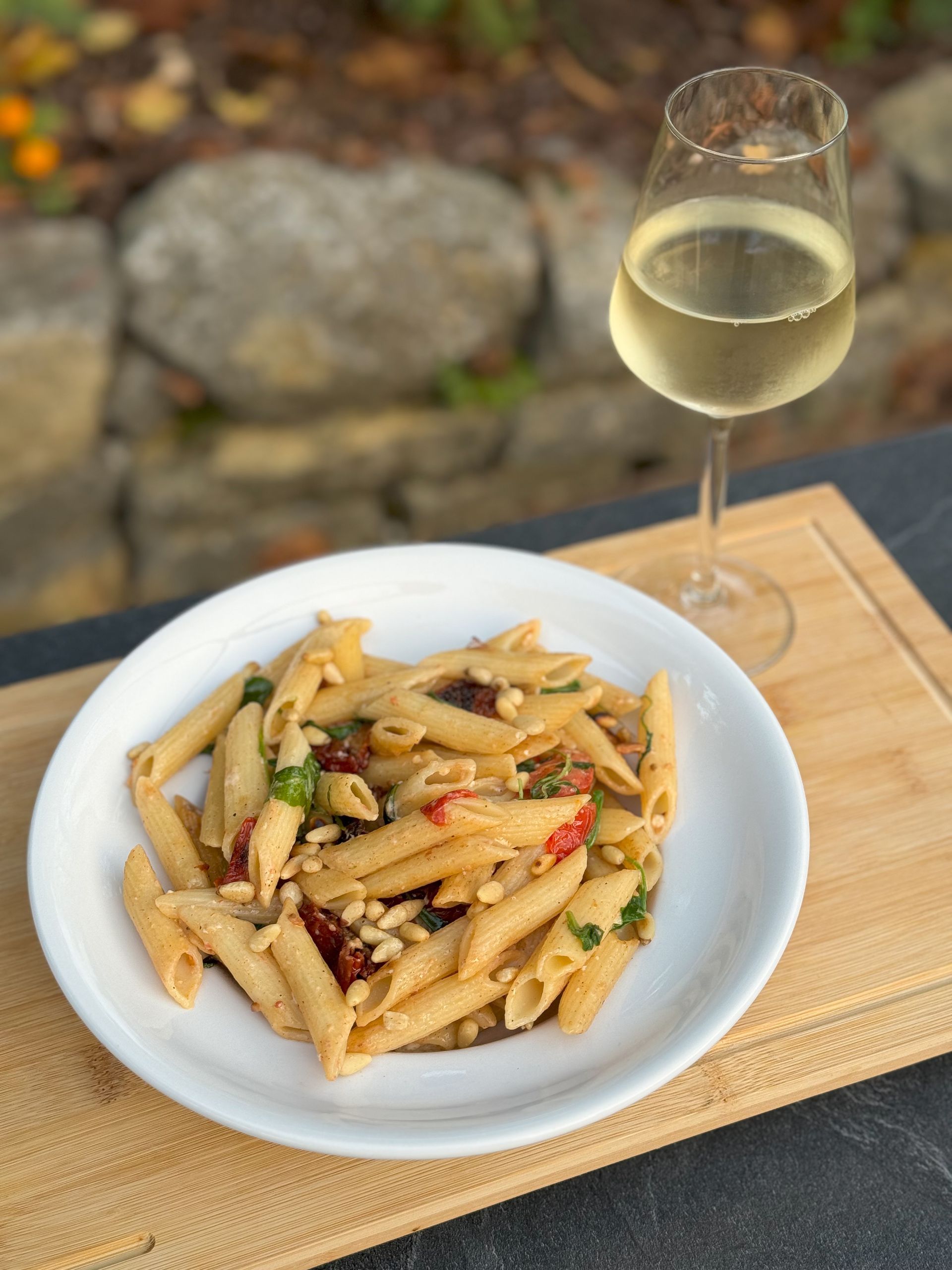 Ein Teller Pasta und ein Glas Wein auf einem Schneidebrett.