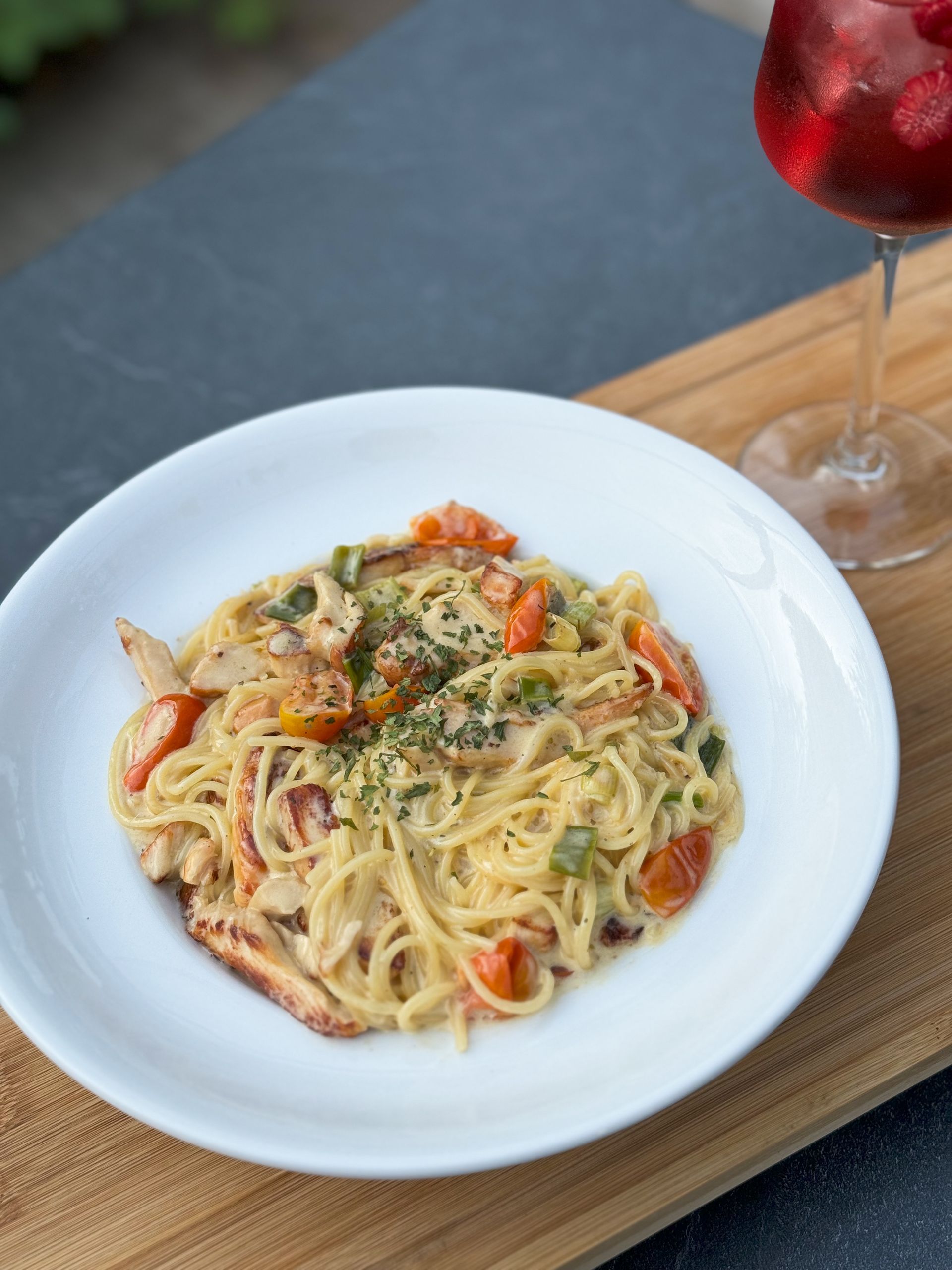Ein weißer Teller mit Spaghetti und Tomaten neben einem Glas Wein.