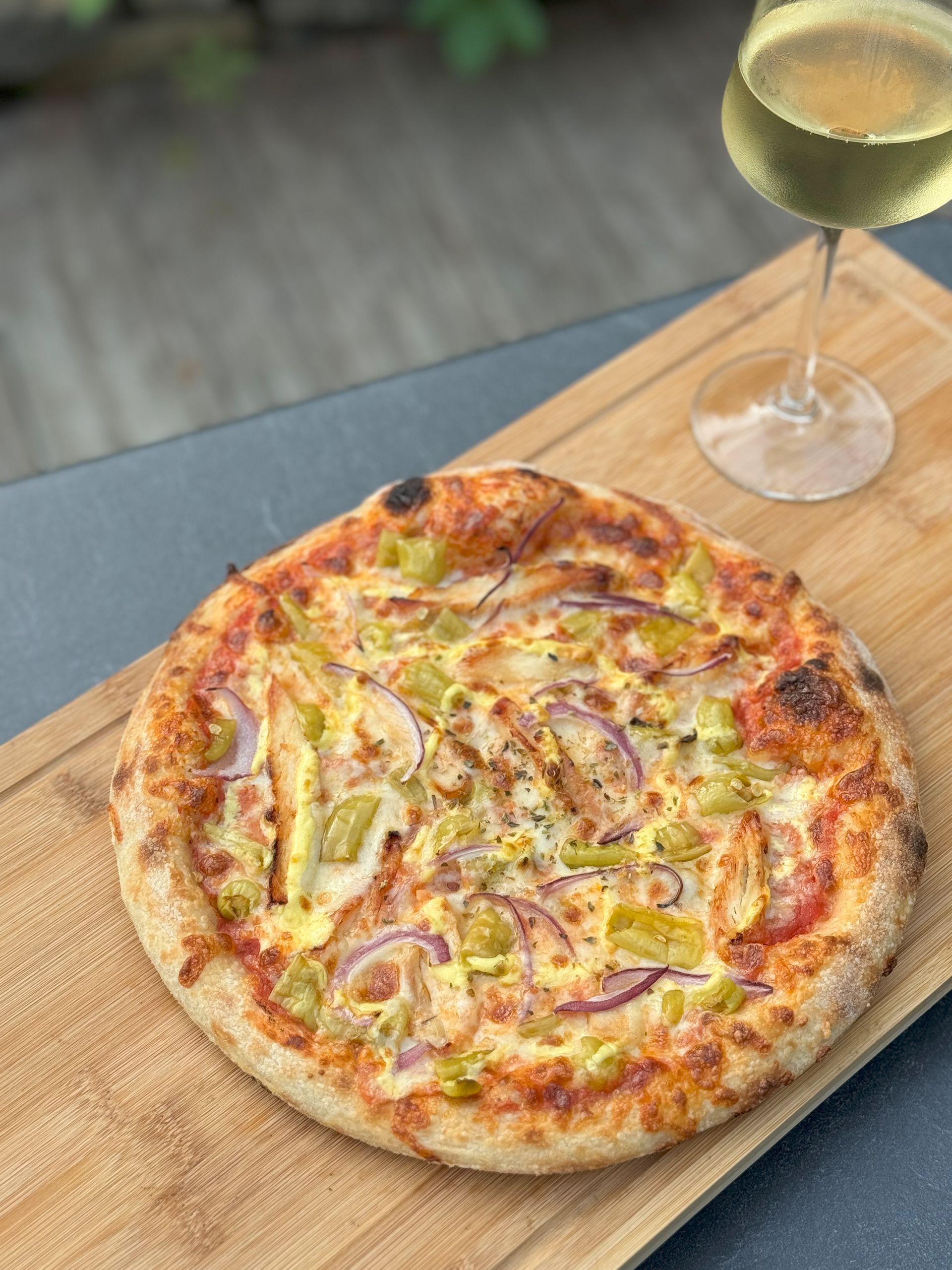 Eine Pizza liegt auf einem Holzschneidebrett neben einem Glas Wein.