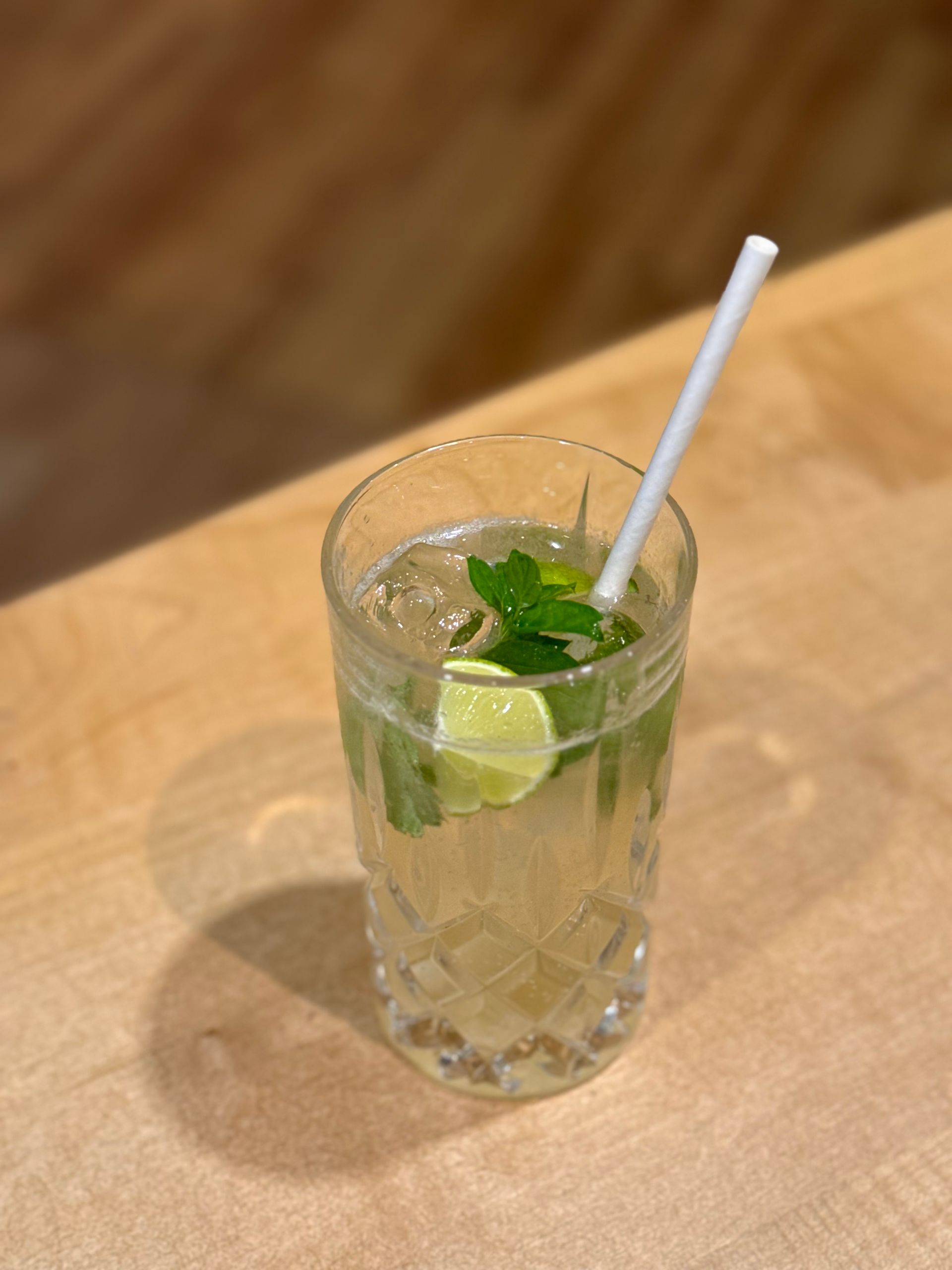 Ein Glas Mojito mit einem Strohhalm auf einem Holztisch.