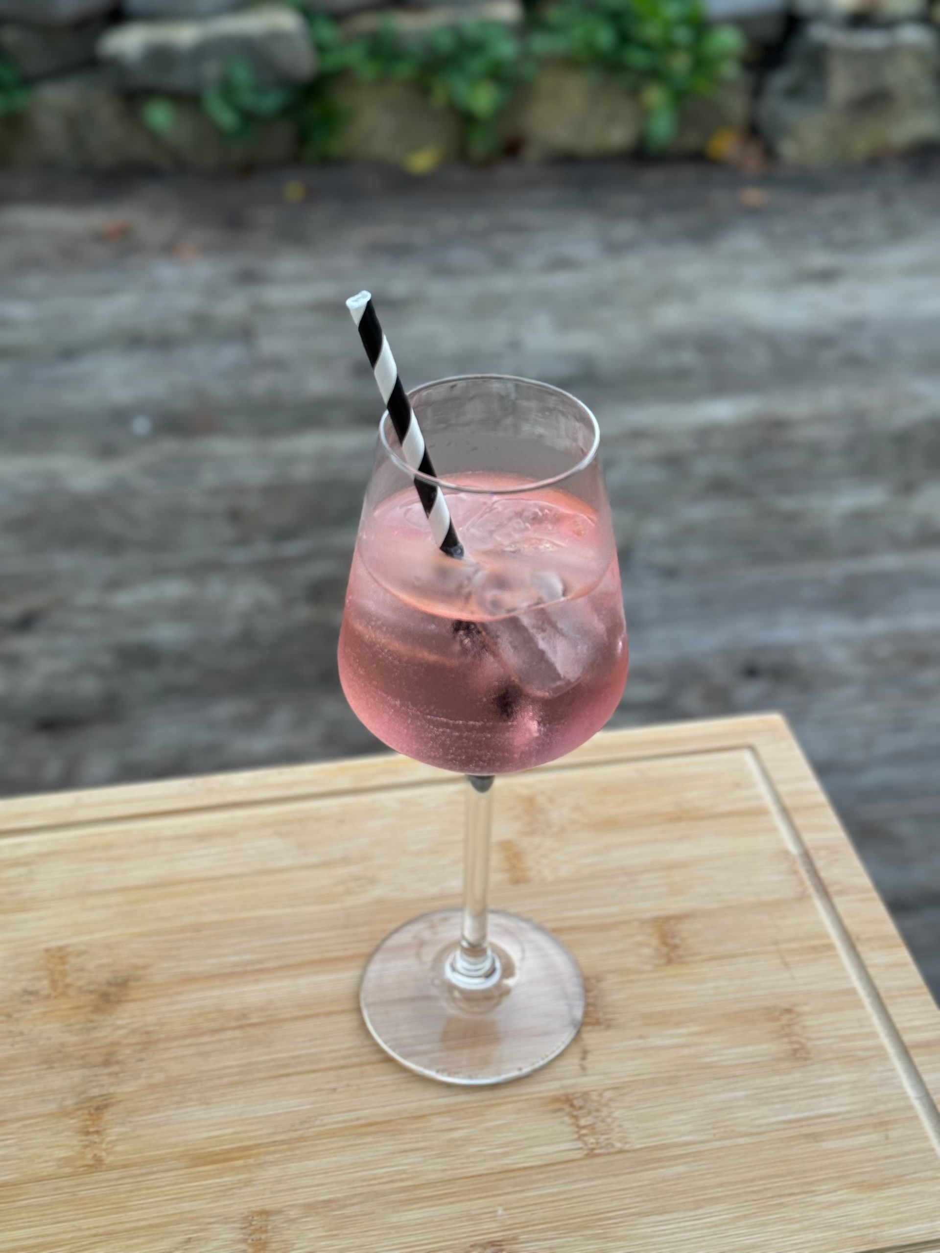 Ein Glas mit rosa Flüssigkeit, Eis und einem Strohhalm auf einem Holztisch.