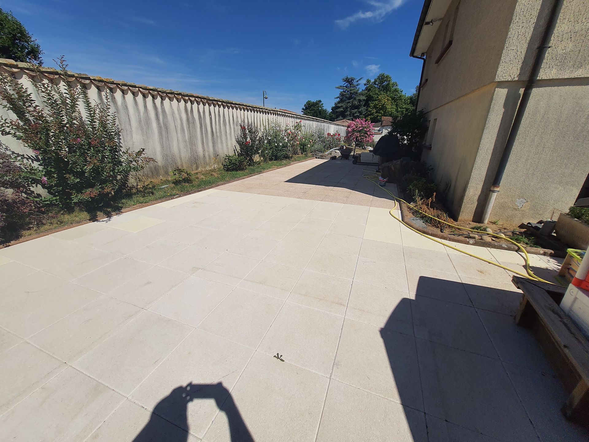 Terrasse pavée jouxtant une maison et un mur en béton par une journée ensoleillée.