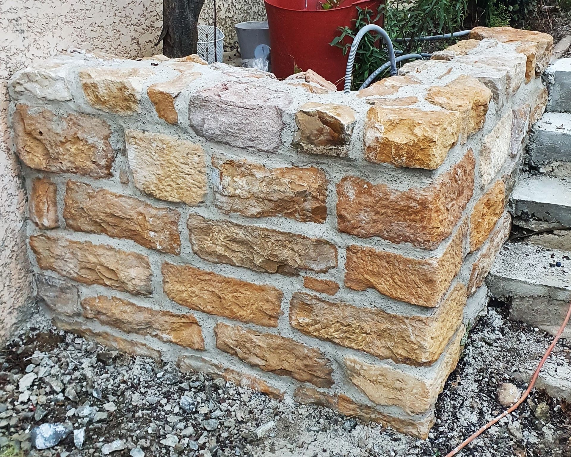 Coin de mur en pierre, pierres beiges et brunes, jointoyées, construction extérieure.