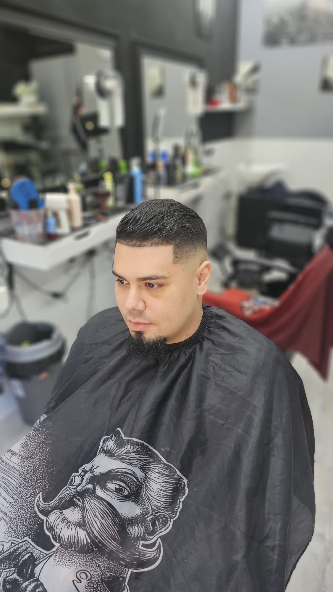 Una persona con capa de barbero y un corte de pelo corto y degradado, sentada en una silla de peluquería.