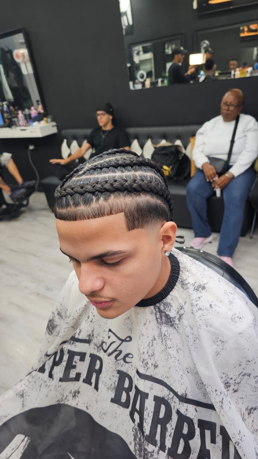 Un cliente de una barbería, que lleva una capa, muestra un corte de pelo recién 