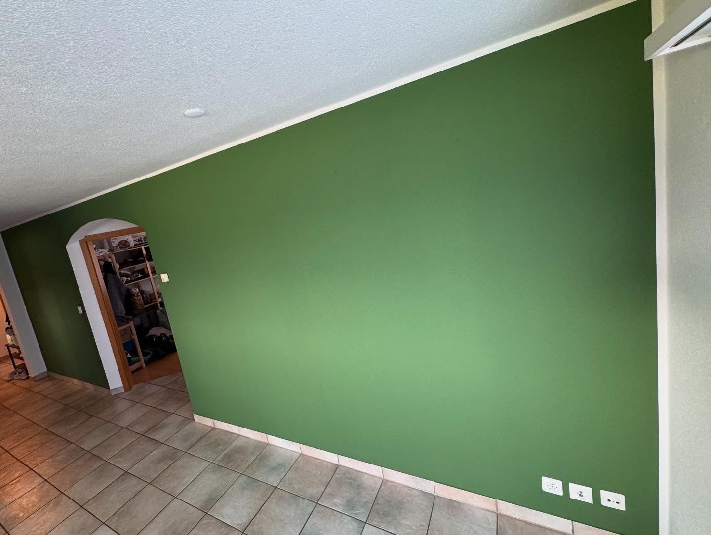 Person, die mit einem Pinsel weiße Zierleisten um ein Fenster streicht.