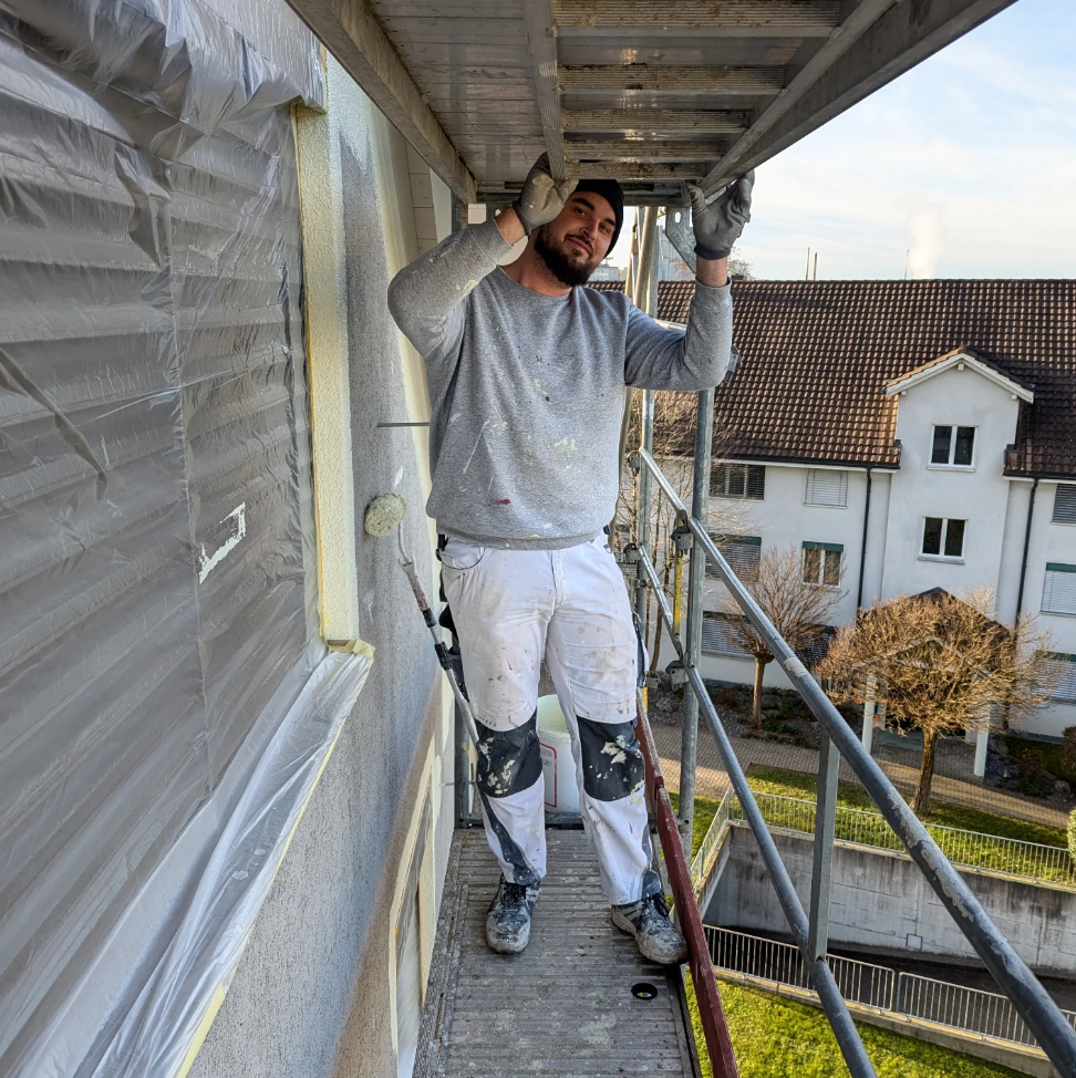 Modernes weißes Betonhaus mit großen Glasfenstern, heller Terrasse und blauem Himmel.
