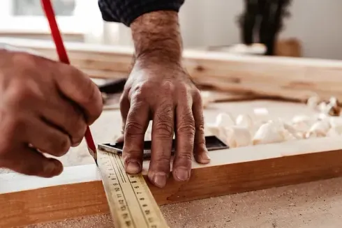 Carpintero midiendo y marcando madera con una regla y un lápiz, de cerca.