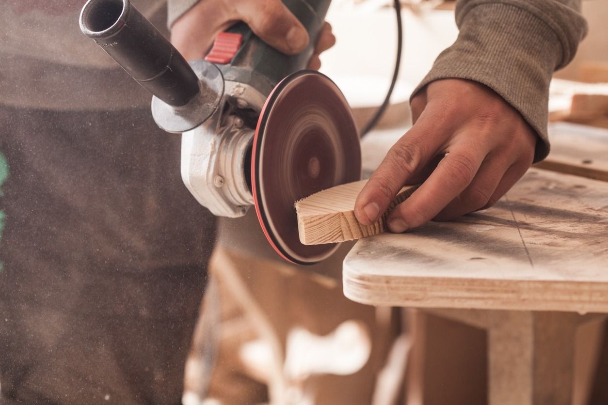 Una persona lijando un trozo de madera con una amoladora eléctrica, generando polvo.