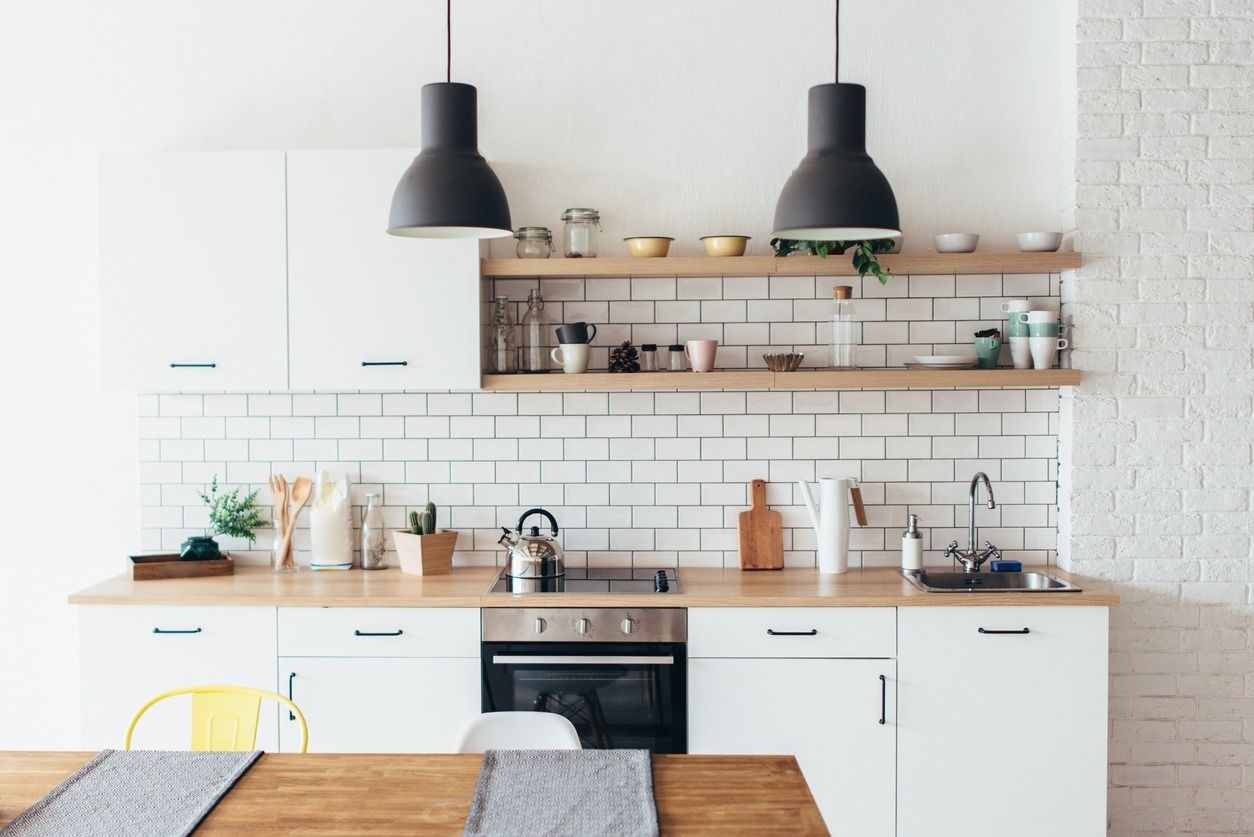 Cocina moderna con gabinetes blancos, encimeras y estantes de madera, protector contra salpicaduras de azulejos del metro y luces colgantes negras.