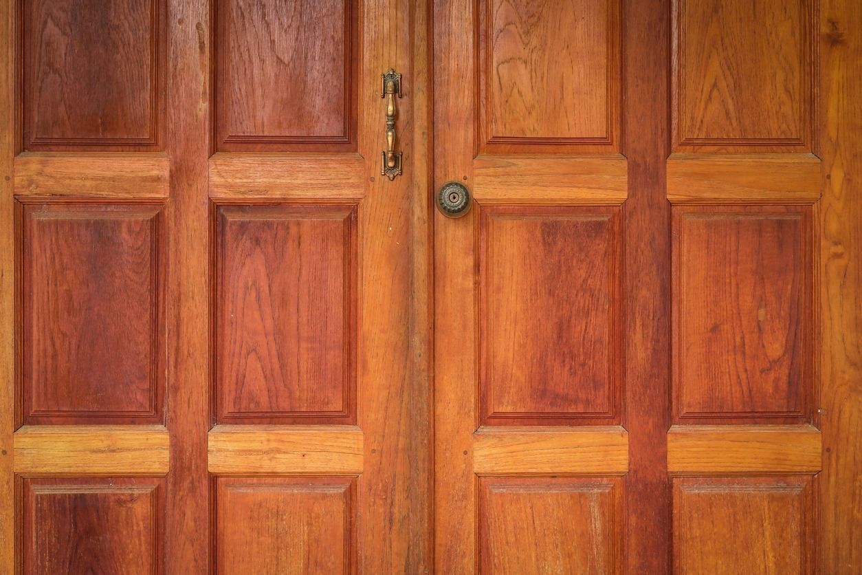 Puertas dobles de madera, tonos marrones y naranjas, con tiradores ornamentados y pomo central.
