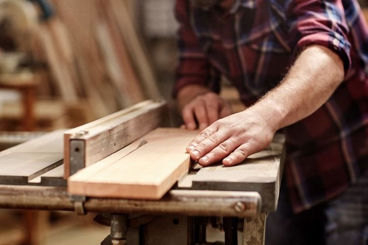 Un carpintero utiliza una sierra de mesa para cortar una tabla de madera en un taller.