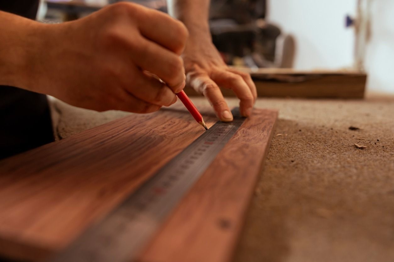 Persona que utiliza una regla y un lápiz para marcar una línea en una tabla de madera.
