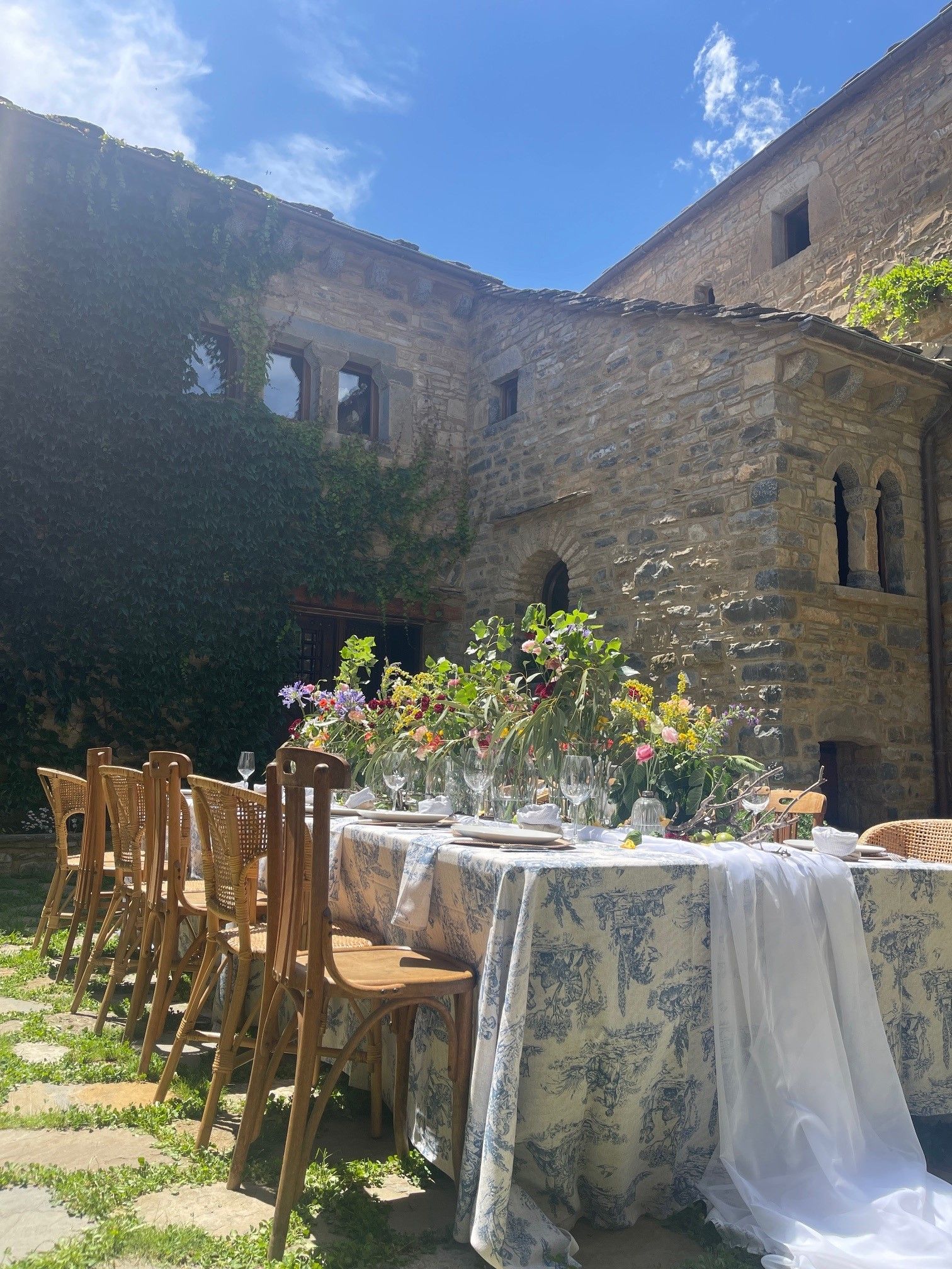 Una mesa larga con sillas y flores delante de un edificio de piedra.