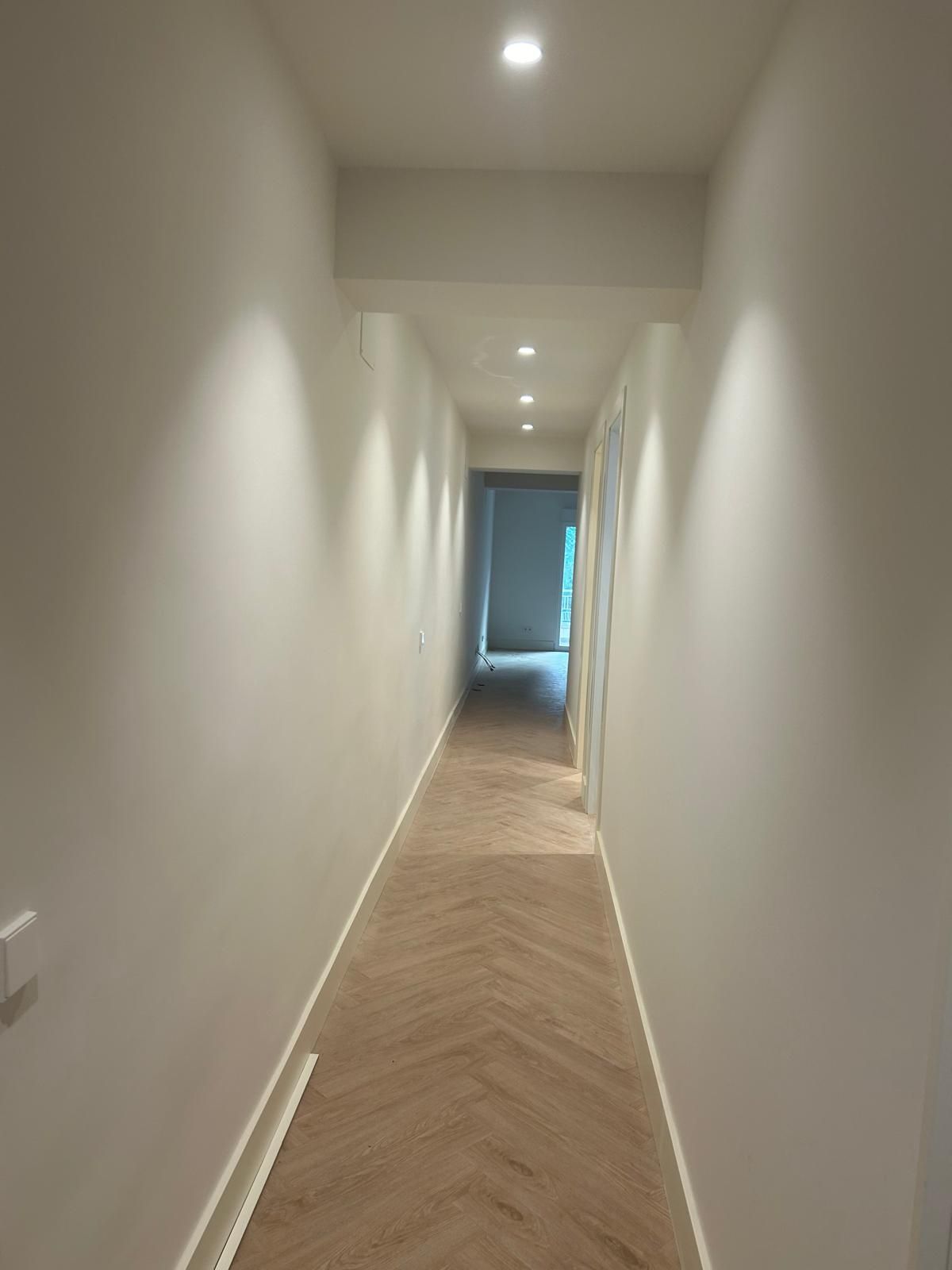 Un largo pasillo con suelo de madera y paredes blancas.