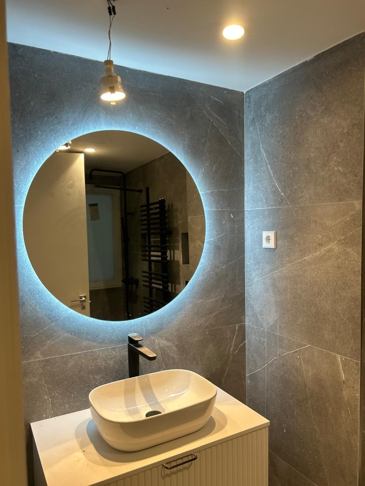 Un baño con lavabo y espejo redondo.