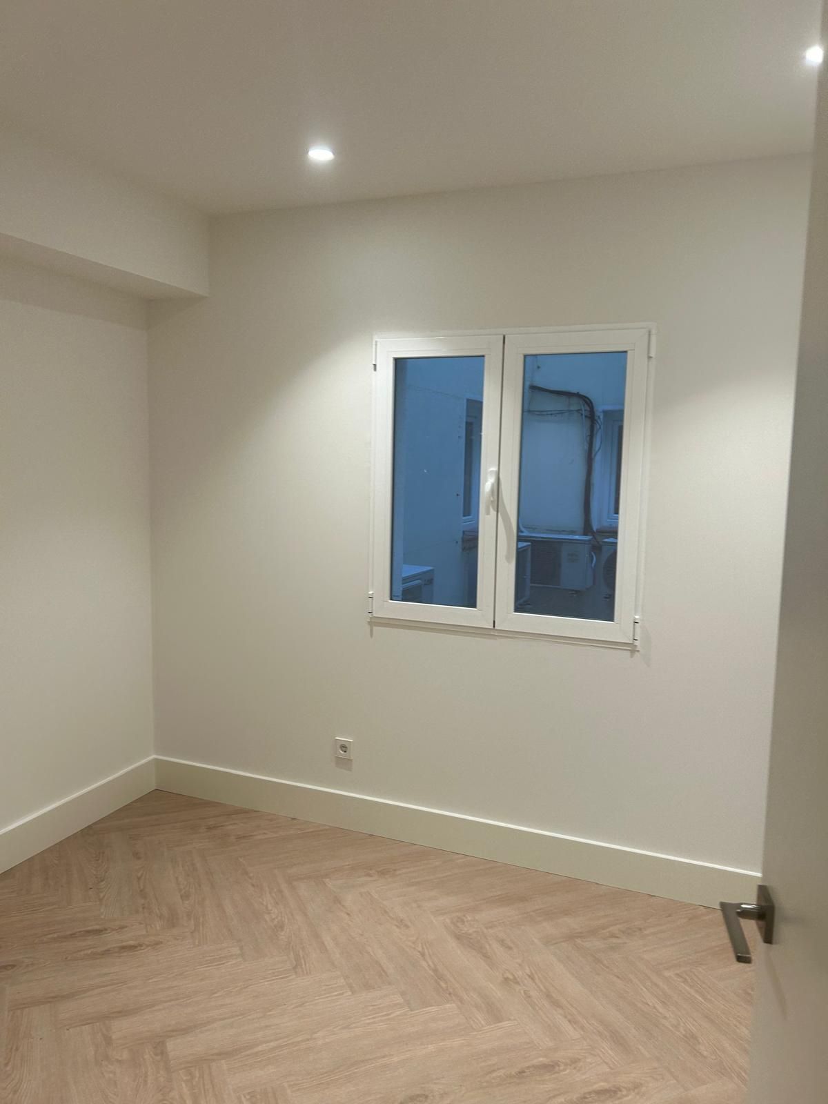 Una habitación vacía con dos ventanas y suelo de madera.