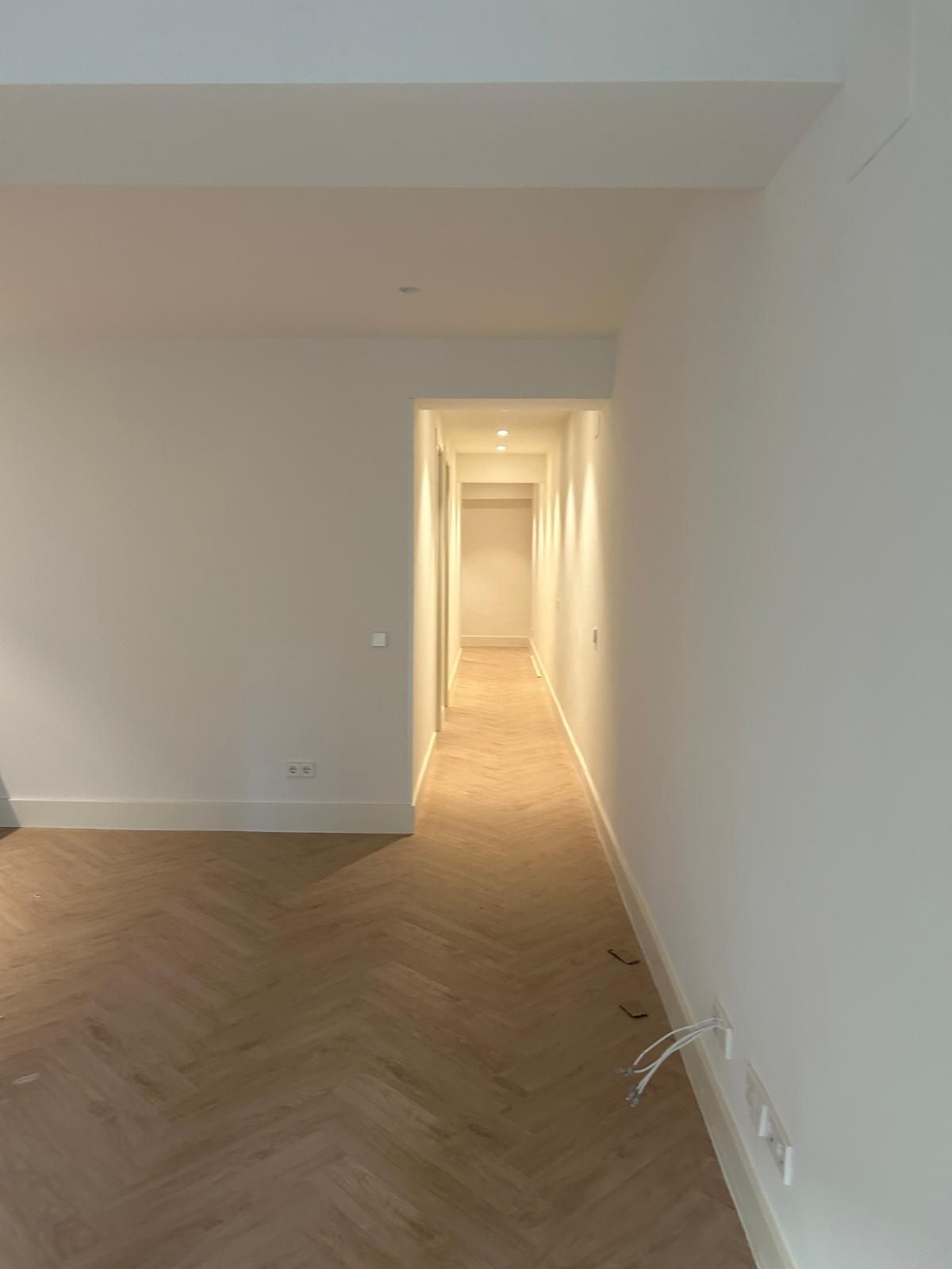 Un pasillo vacío con suelo de madera y paredes blancas.