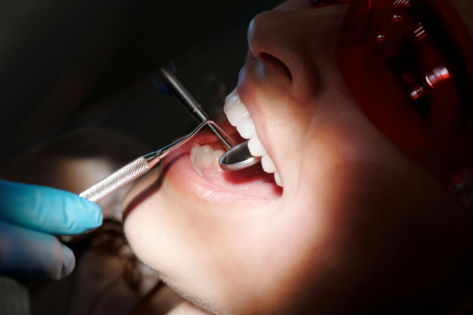 Pessoa no dentista com a boca aberta, sendo examinada com instrumentos odontológicos.