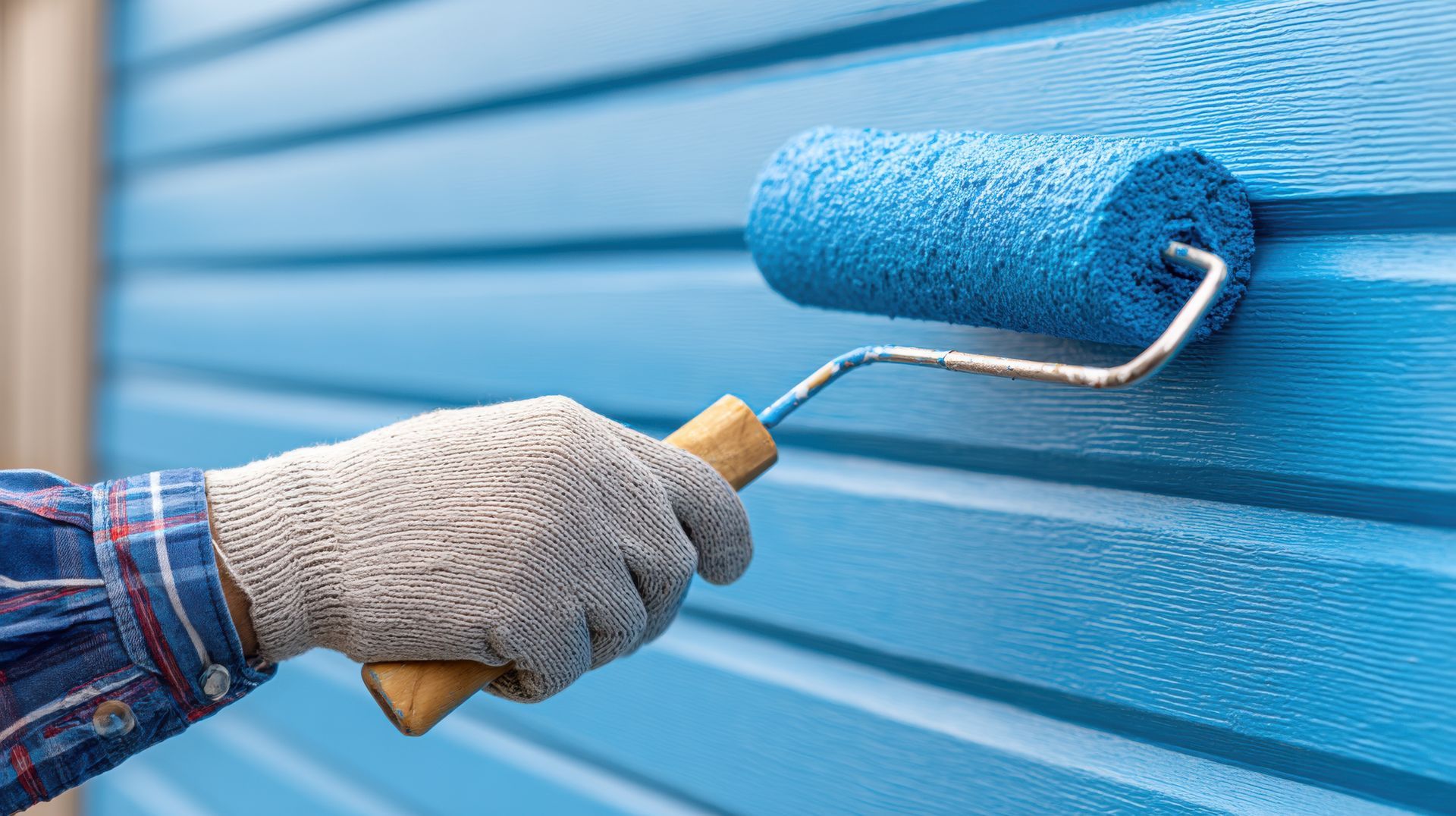 Main avec un rouleau à peinture appliquant de la peinture bleue sur le revêtement.