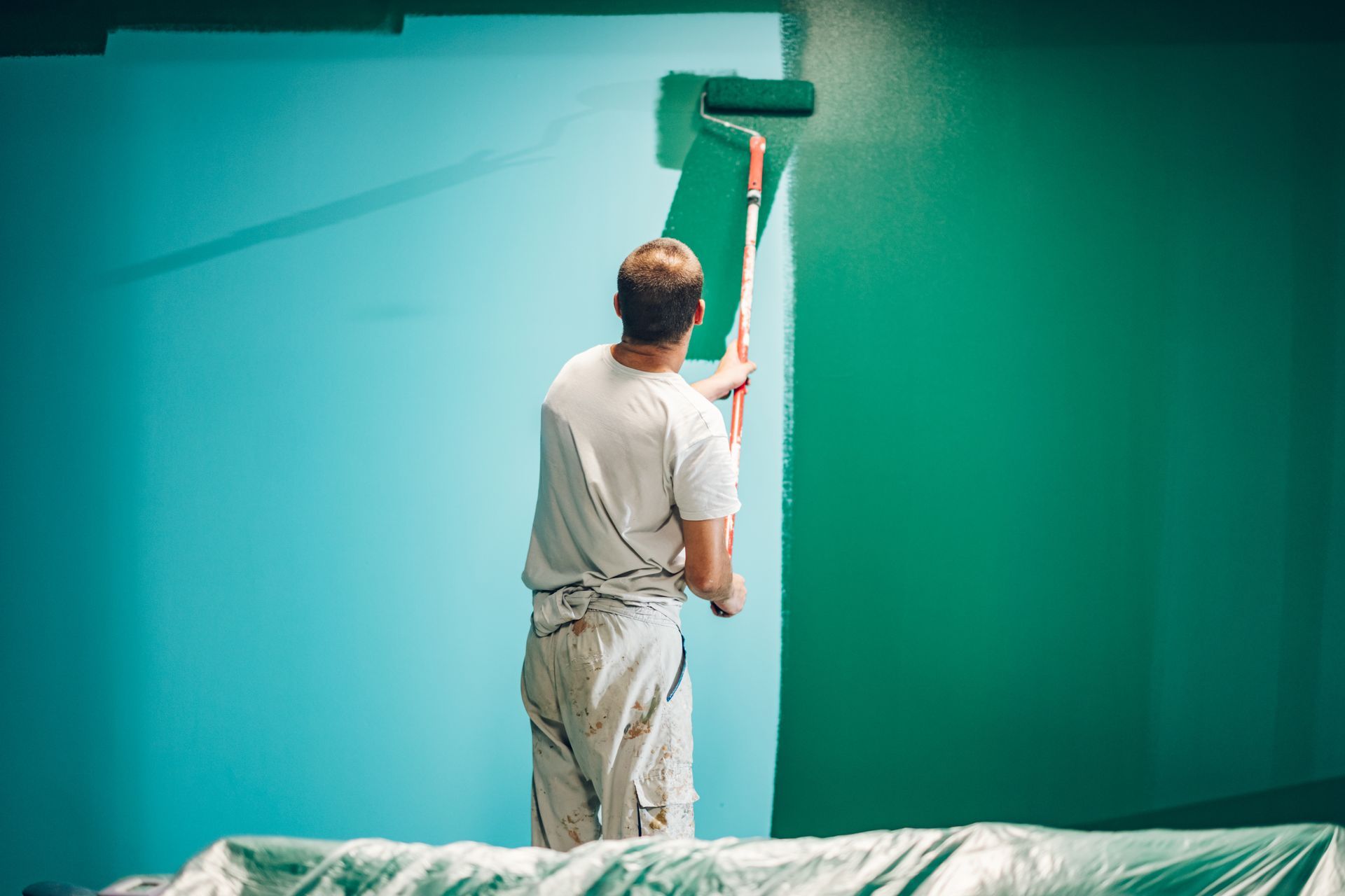 Une personne peint un mur en vert avec un rouleau ; l’autre mur est bleu clair.