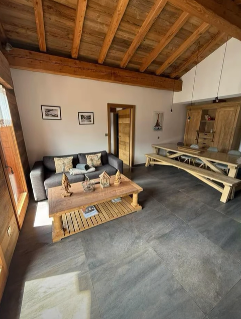 Salon avec parquet gris, poutres en bois, un canapé gris, une table en bois et une grande table à manger.