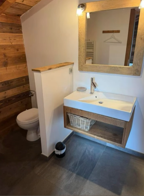 Salle de bain avec un lavabo flottant moderne, des toilettes, des accents de bois et un miroir.