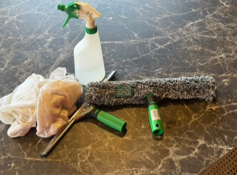 Fournitures de nettoyage de vitres : vaporisateur, applicateur de lavage, raclette, gants, sur une surface à motif marbré.