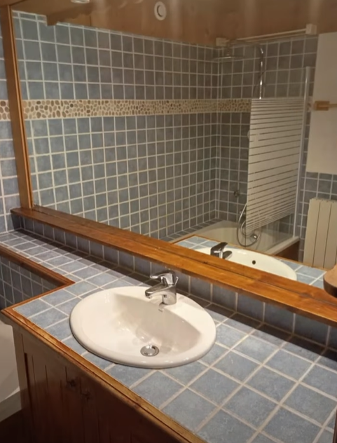 Salle de bain avec murs carrelés bleus, un lavabo et un miroir.