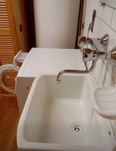 Évier utilitaire blanc avec robinet chromé, à côté d'une machine à laver dans une buanderie.