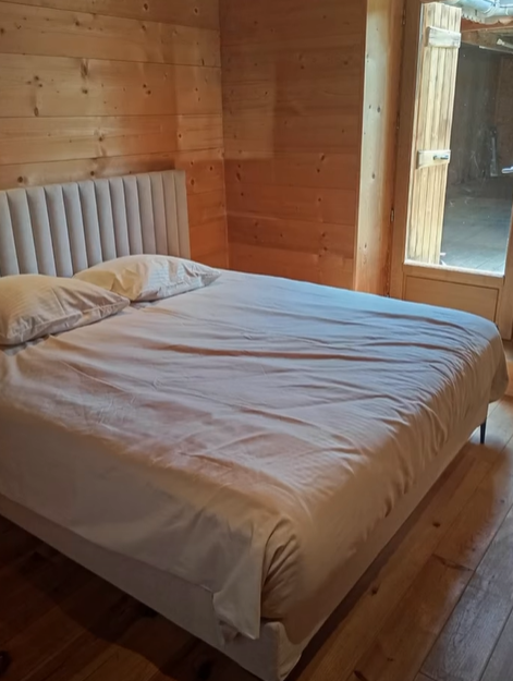 Chambre avec un lit, une tête de lit, une literie claire, des murs et un sol en bois. Porte apparente.