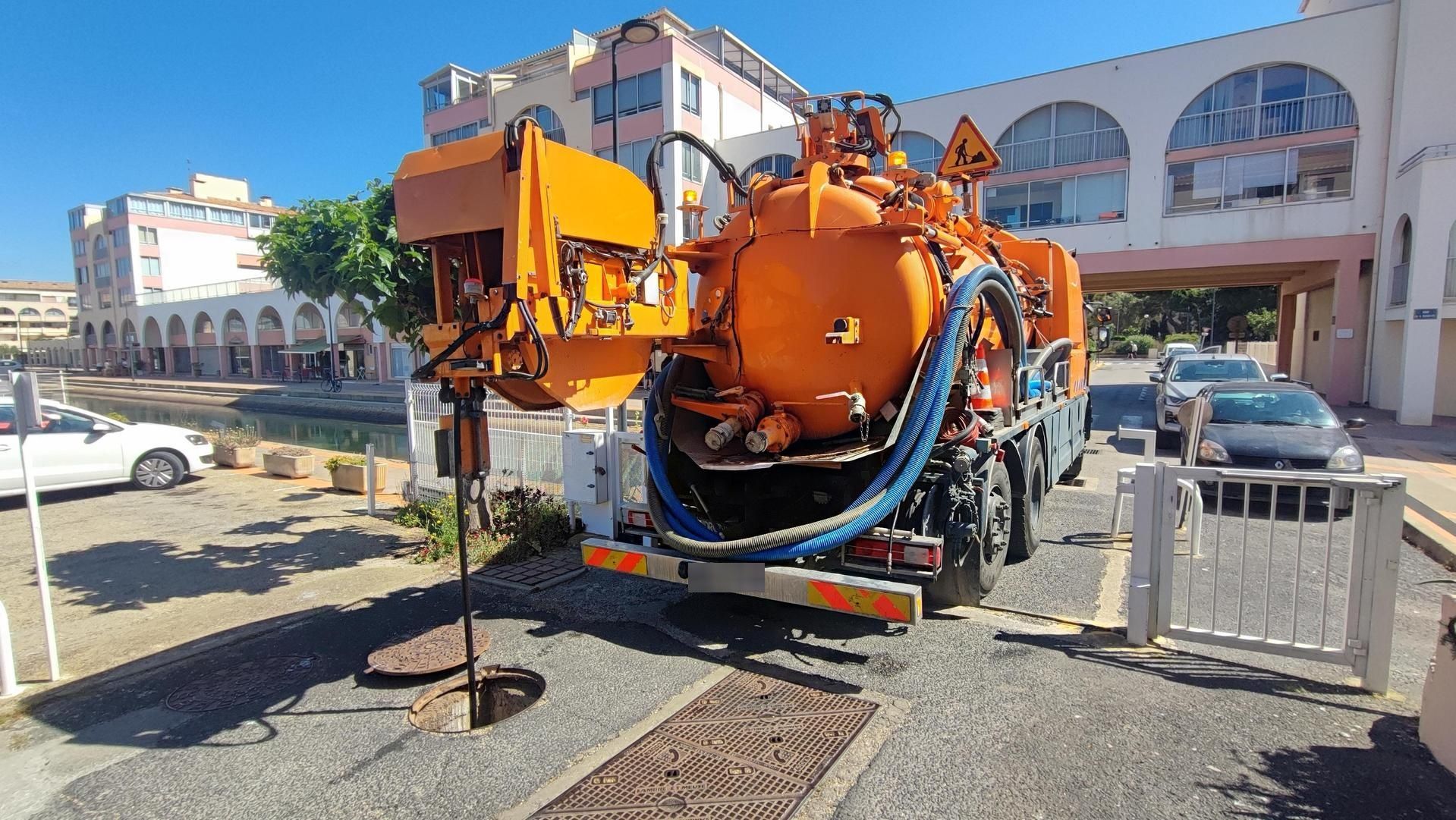 Camionnette utilitaire orange avec équipement arrière garée dans une rue à côté de bâtiments et de voitures stationnées