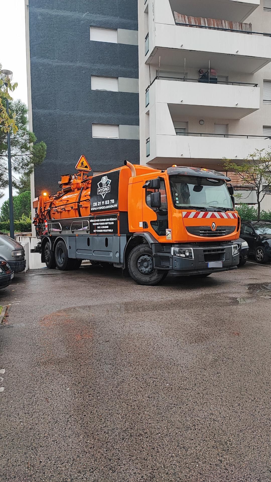 Camion-citerne orange sur une rue mouillée, à côté d'immeubles d'habitation, avec des employés sur la plateforme arrière.