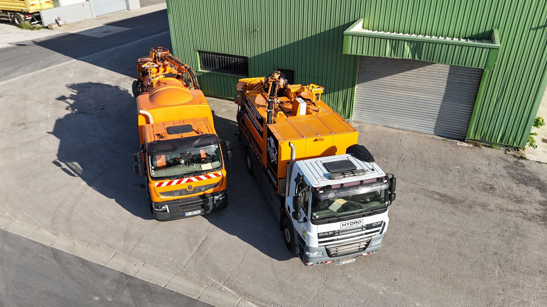 Un ouvrier en manches bleues raccorde un tuyau à un camion-citerne orange.
