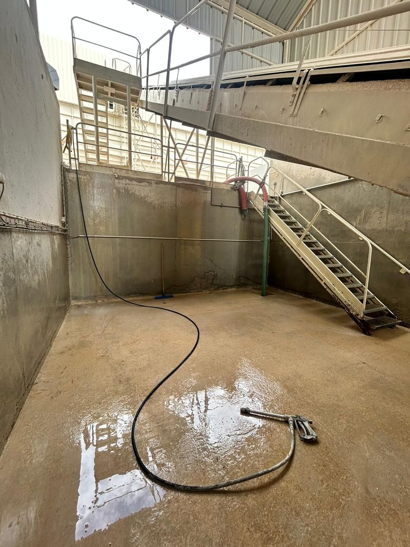 Zone de stockage de réservoirs industriels avec sol humide, tuyaux, murs en béton et escalier métallique sous une structure couverte