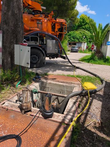 Camion utilitaire orange près d'un regard d'égout ouvert, avec des tuyaux et des câbles dans une cour en gravier