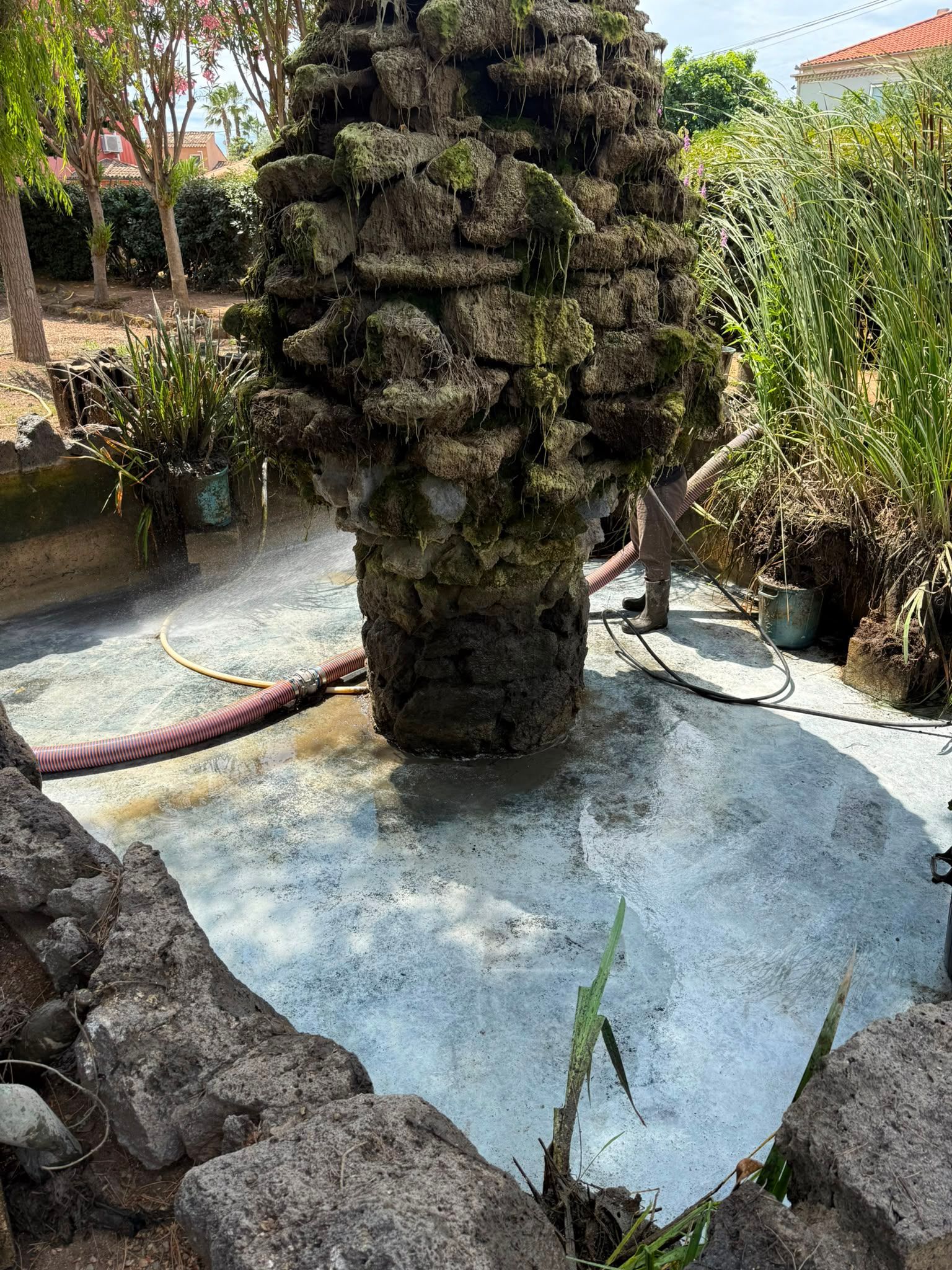 Fontaine en pierre avec pilier en pierre brute et bassin d'eau peu profond dans un cadre de jardin
