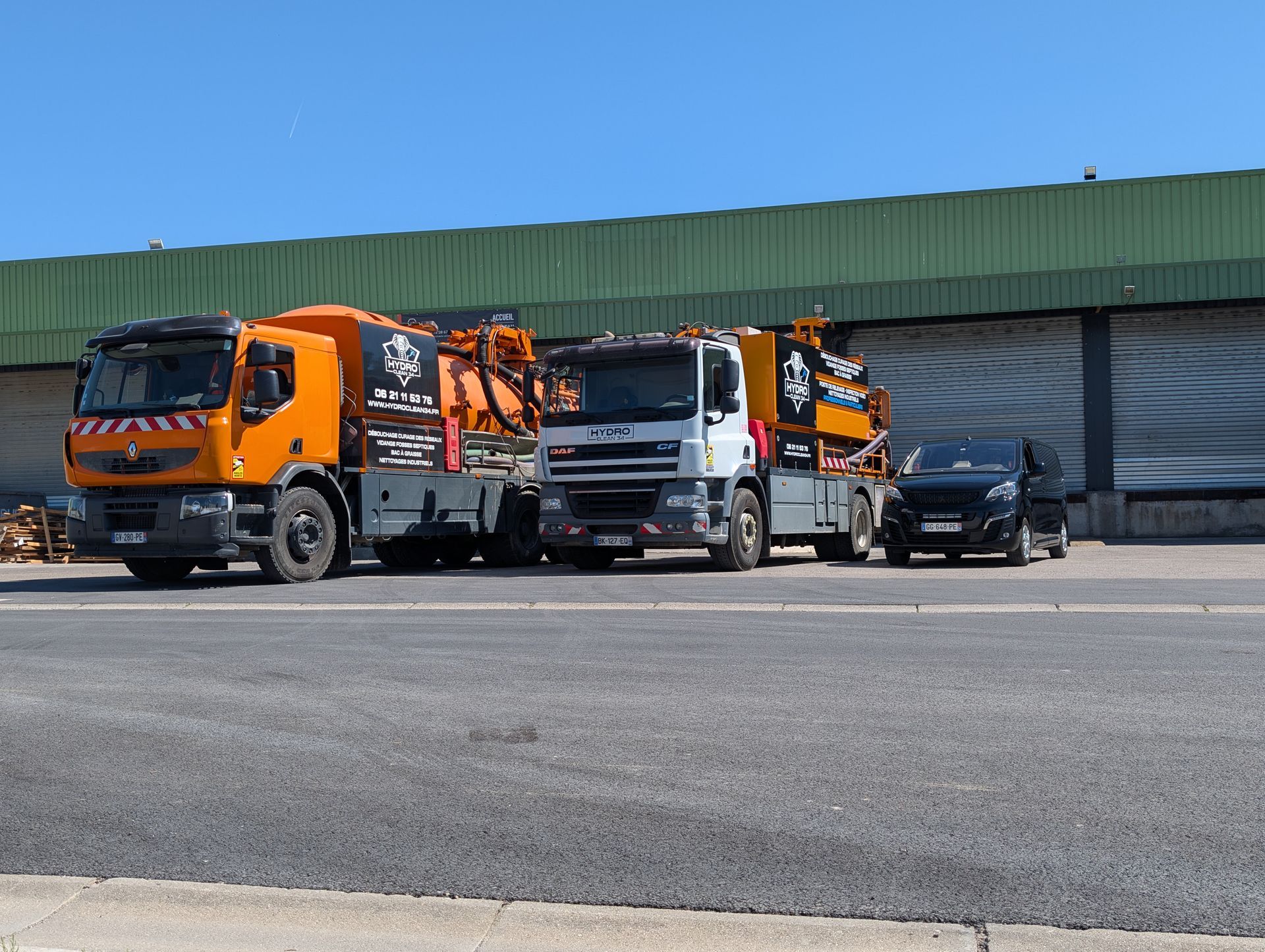 Deux camions et une voiture noire étaient garés devant un entrepôt.