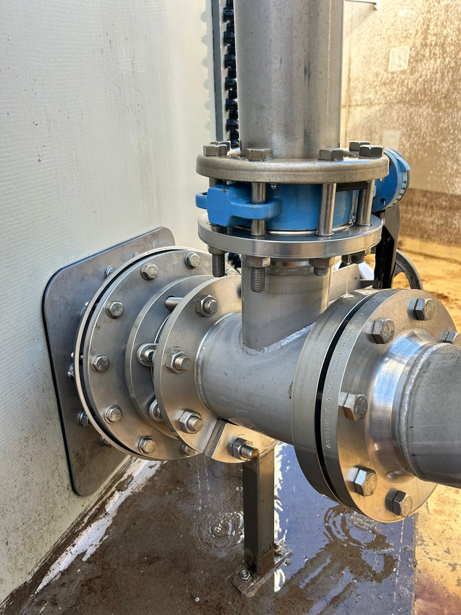 Trappe ouverte d'un réservoir bleu contenant un tuyau et un seau, laissant apparaître un résidu liquide brunâtre