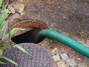 Un tuyau vert a été inséré dans une ouverture de drainage souterraine ronde, à côté d'une plaque d'égout extérieure.