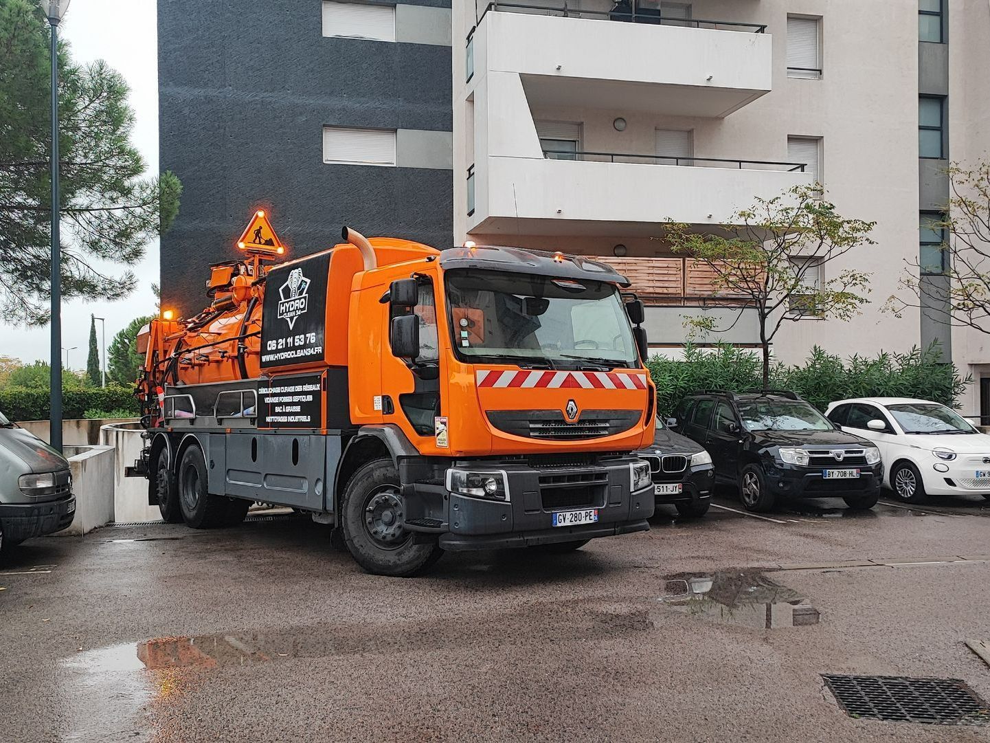 Camionnette utilitaire orange garée dans une rue mouillée, à côté d'immeubles et de voitures stationnées
