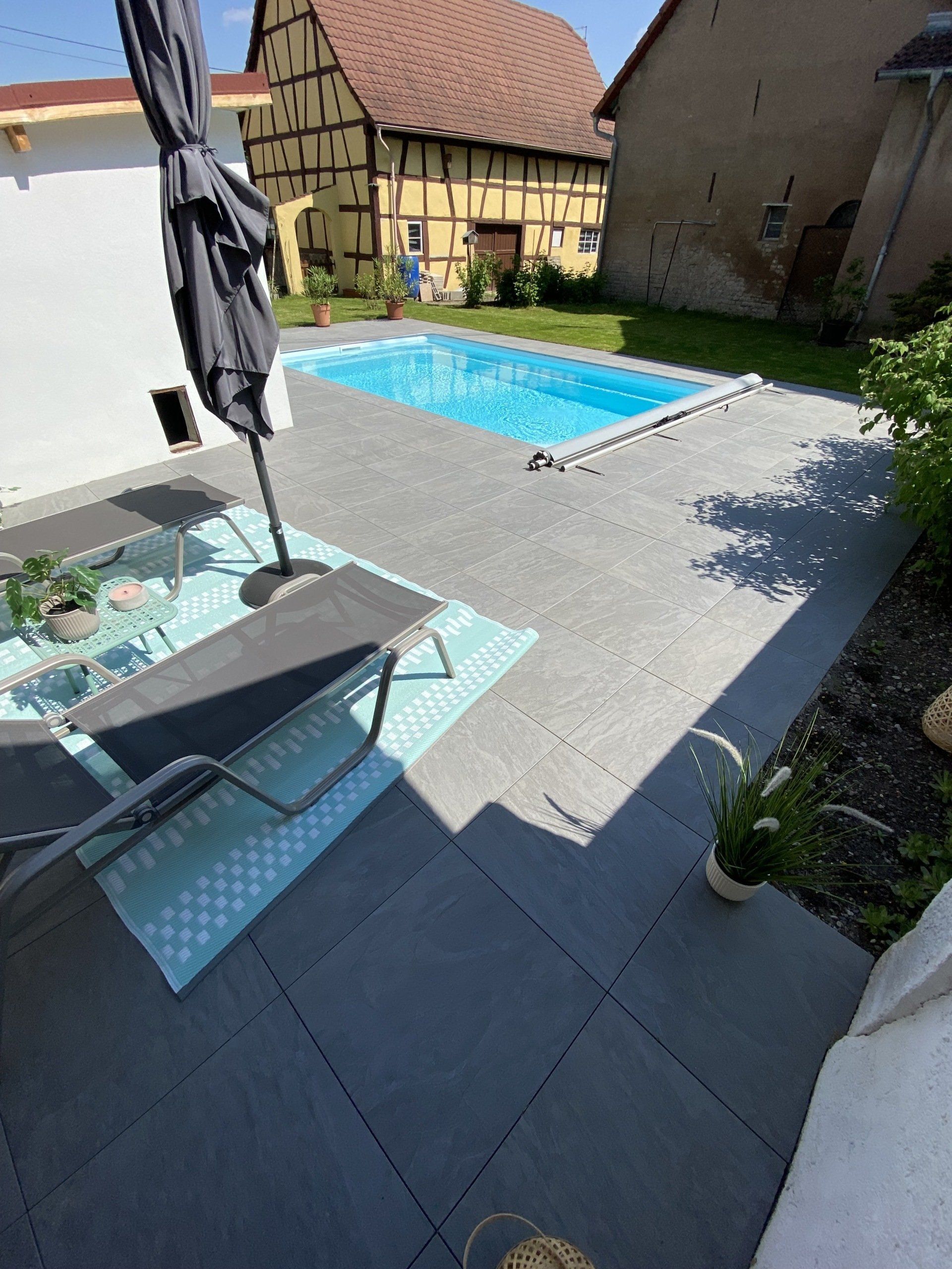 Cour arrière avec piscine, patio, parasol, chaise longue et bâtiments historiques à colombages.