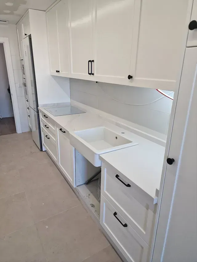 Una cocina con gabinetes blancos, un fregadero y un refrigerador.