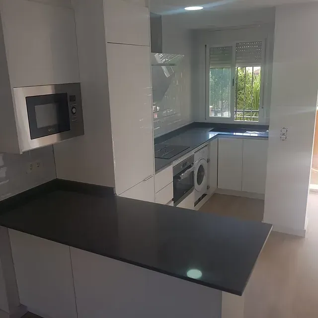 Una cocina con gabinetes blancos, encimeras negras, lavadora y secadora y un microondas.